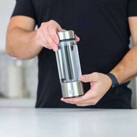 AquaFusion bottle held in two hands over a kitchen counter, the stainless base and its round button facing the camera